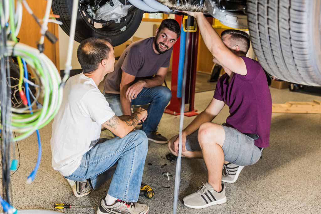 Three men working underneath a vehicle
