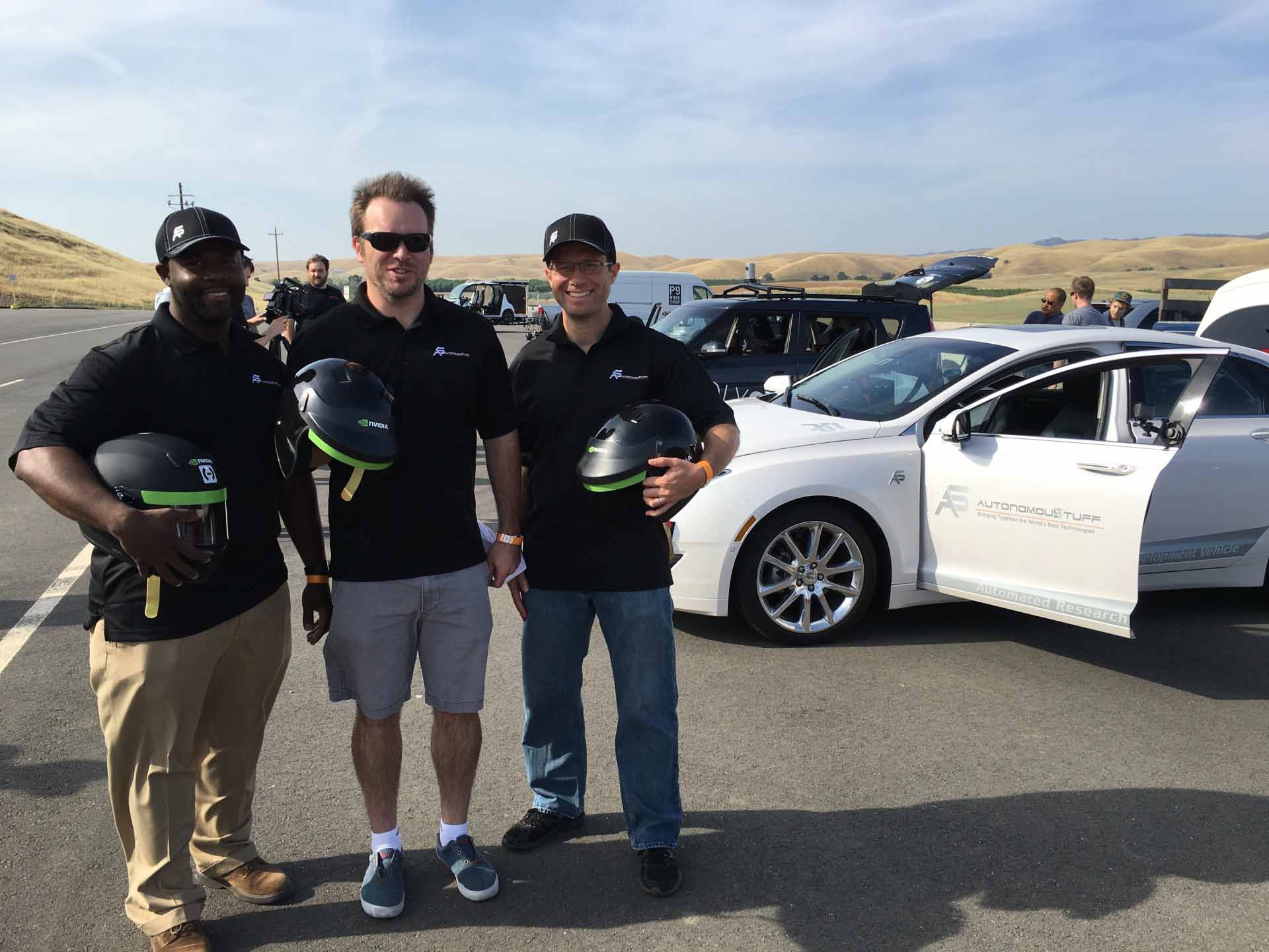 Three men posing in front of cars
