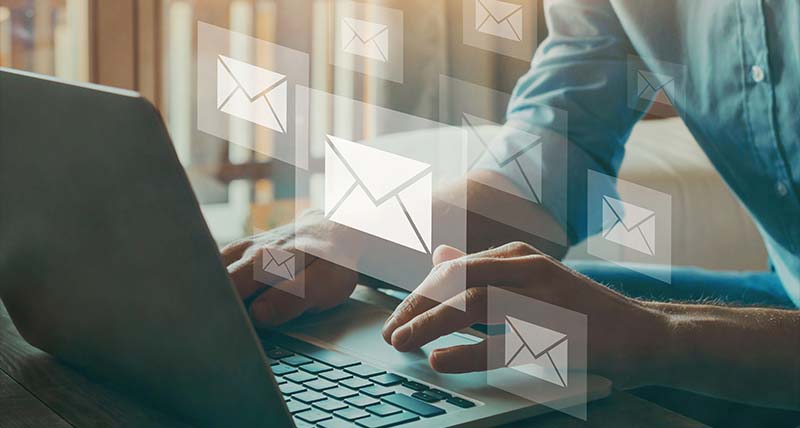 Man typing on a laptop with floating envelope icons